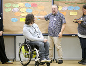 Vier Menschen, einer davon im Rollstuhl, diskutieren vor einer Pinnwand