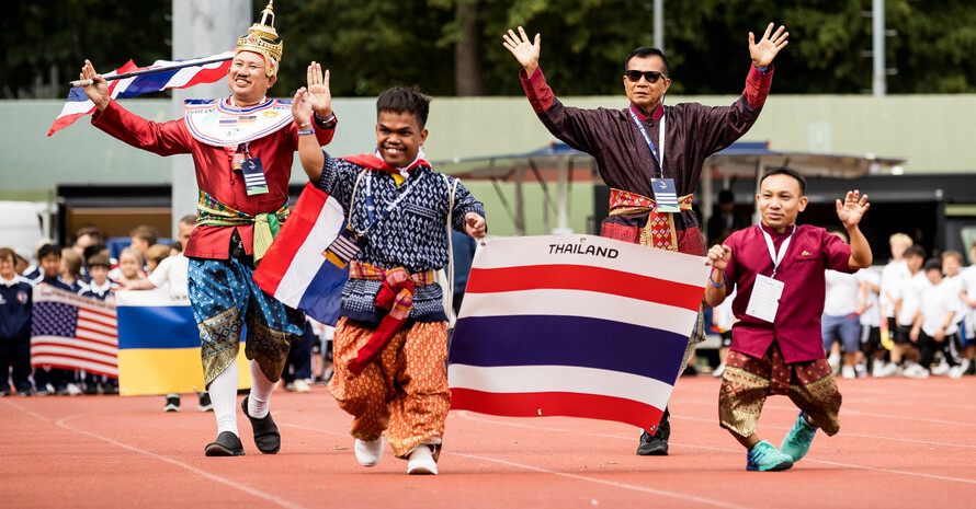 Vier fröhliche Repräsentanten aus Thailand stellen beim Einlaufen stolz ihre Flagge zu schau. Im Hintergrund sind Vertreter der Ukraine und der USA mit ihren Flaggen zu sehen