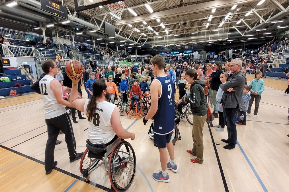 eine Gruppe von Kindern in Rollstühlen wartet darauf, dass ihnen ein Rollstuhl-Basketballspieler den Ball von der Grundlinie aus zuwirft wirft eine Gruppe von Kindern in Rollstühlen wartet darauf, dass ihnen ein Rollstuhl-Basketballspieler den Ball von der Grundlinie zuwirft