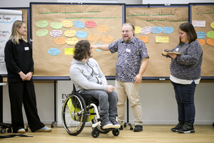 Vier Menschen, einer davon im Rollstuhl, diskutieren vor einer Pinnwand