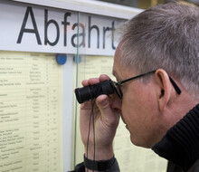 ein Mann mit Lupe versucht die Aushänge der Bahn zu lesen