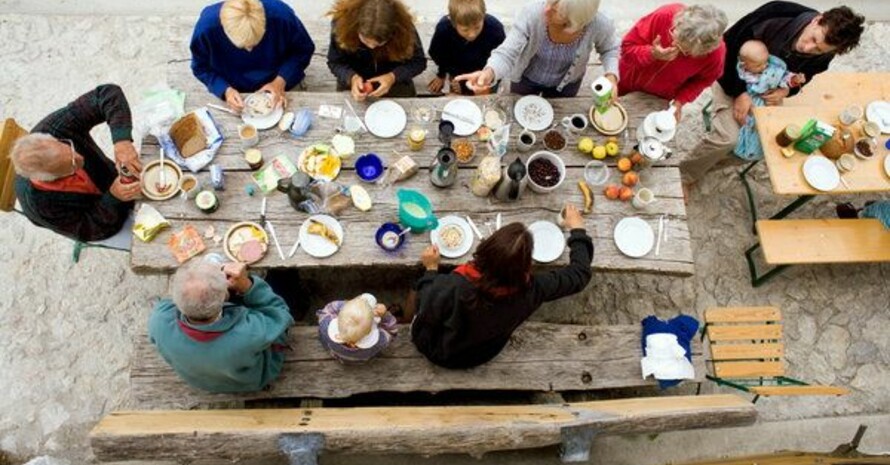 Eine Großfamilie frühstückt vor einer Hütte in den bayerischen Alpen. Foto: picture-alliance