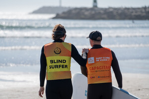 Ein Surfer und sein Coach machen sich am Strand auf dem Weg in Richtung Meer. 