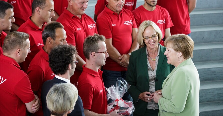 Leichtathlet Sebastian Kröger, Athletensprecher der Deutschen Delegation, überreichte Bundeskanzlerin Angela Merkel ein Delegationsbuch und ein T-Shirt als Gastgeschenk. Links neben der Kanzlerin steht SOD-Präsidentin Christiane Krajewski (Foto: Bundes