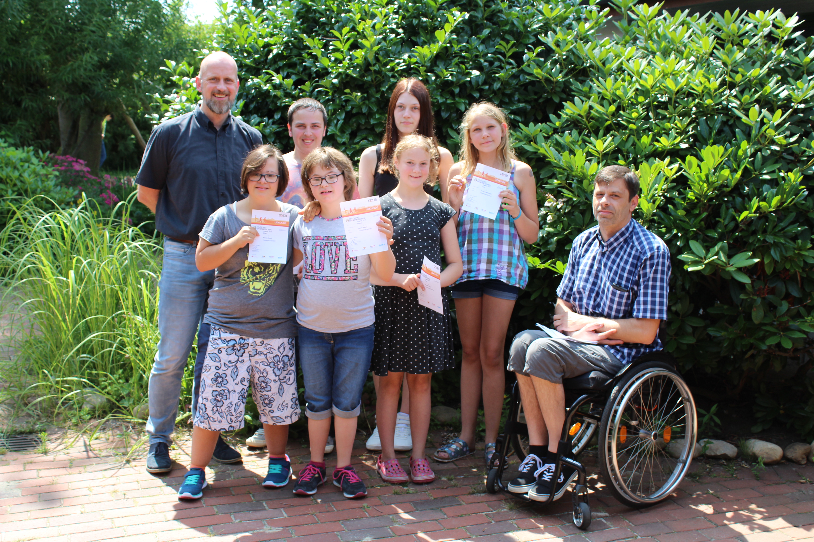 Gruppenfoto der zehn jungen Sportler/innen, die ihre Urkunden in den Händen halten, mit Stefan Doege (Sport-Inklusionsmanager der HpH) und Axel Wichmann (Schulleiter Paul-Moor-Schule). 